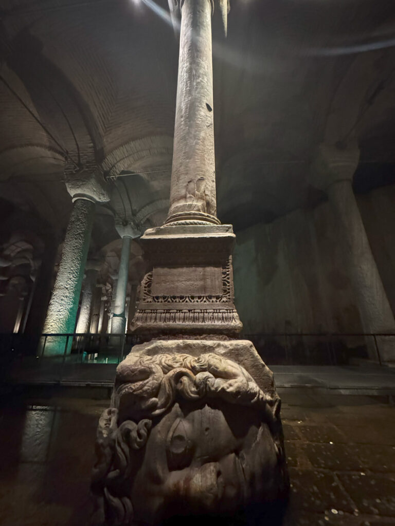 Sideways Medusa Head at the base of a column inside the Basilica Cistern, illuminated under soft light.
