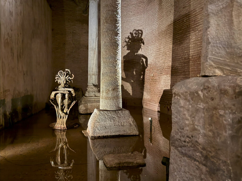 Modern art installations in the side aisle exhibition area of the Basilica Cistern, including glowing jellyfish-like lights and a Medusa sculpture casting dramatic shadows.