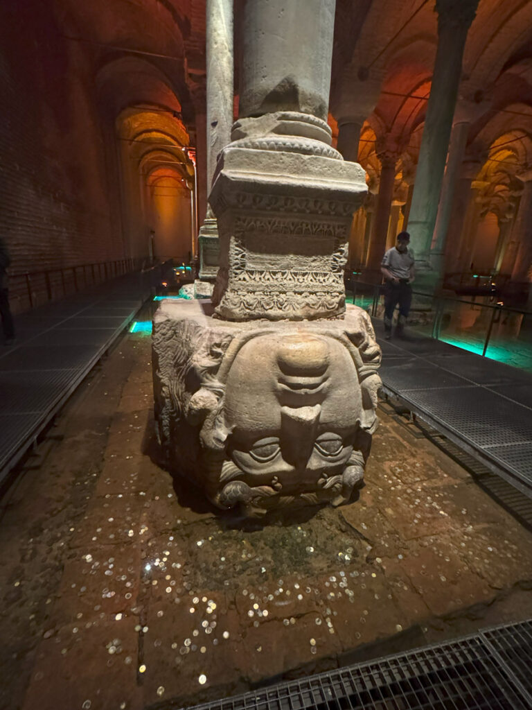 Upside-Down Medusa Head at the base of a column inside the Basilica Cistern, surrounded by shimmering coins left by visitors.