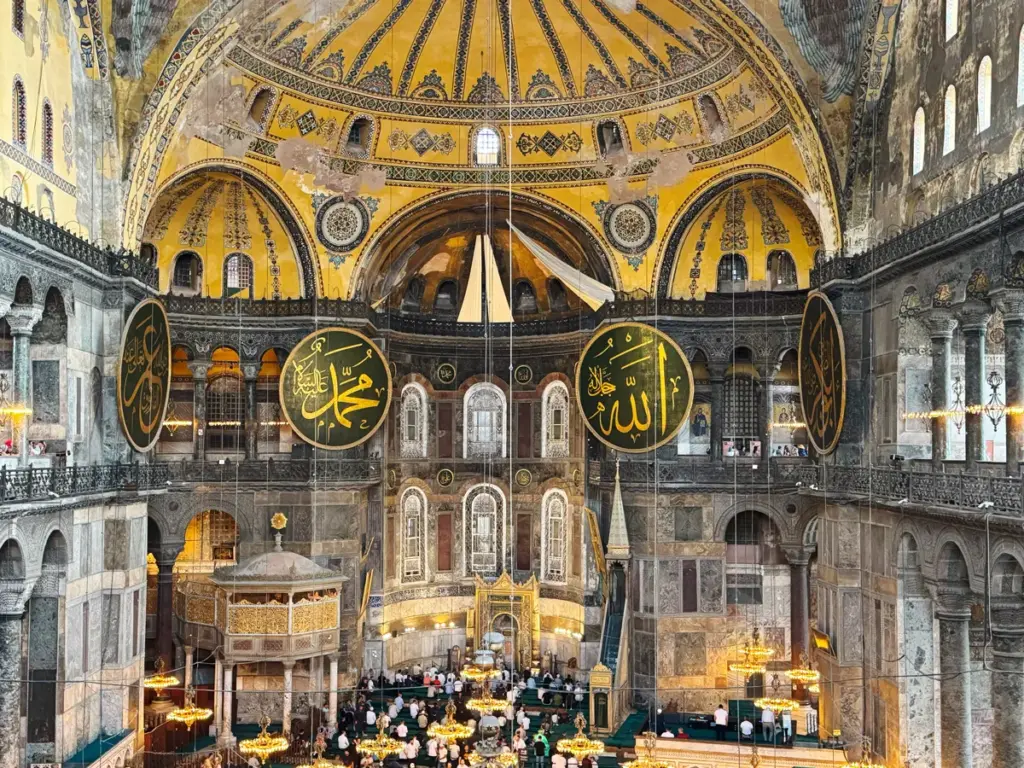 Interior view of the Hagia Sophia in Istanbul, showing the vast golden dome, marble galleries, and large Islamic calligraphy medallions — a symbol of the city’s blend of Byzantine and Ottoman heritage.