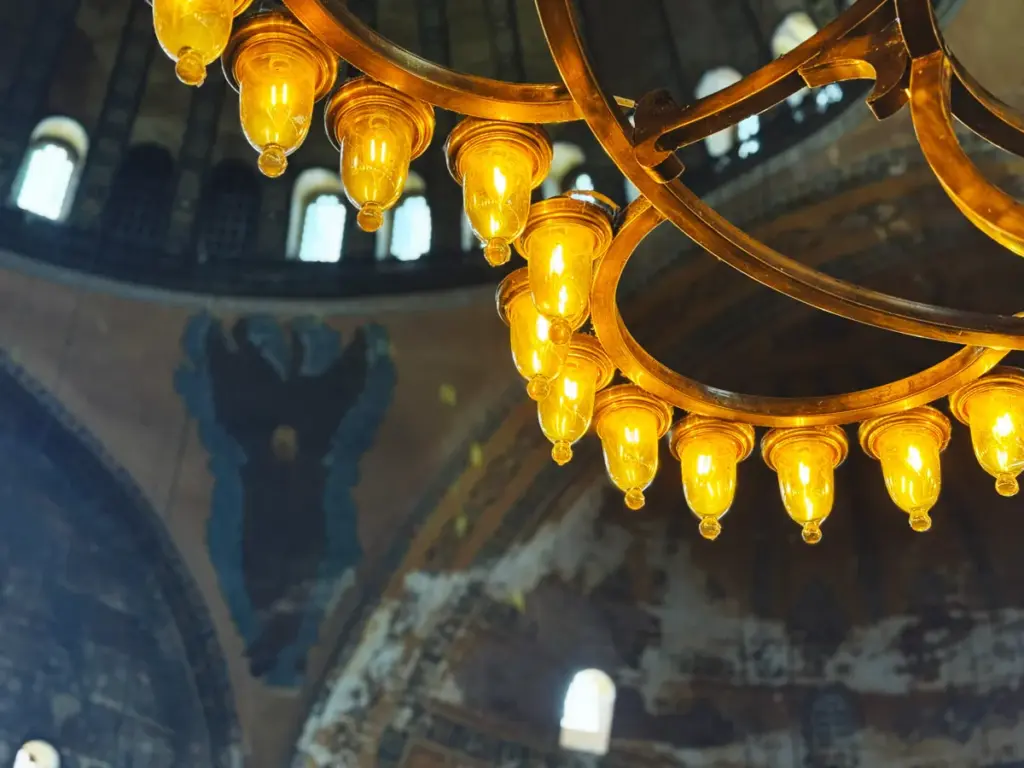 A view of Hagia Sophia’s ceiling from the upper gallery, showing ancient hanging lamps and faint angelic figures that evoke the timeless sacred atmosphere of the monument.
