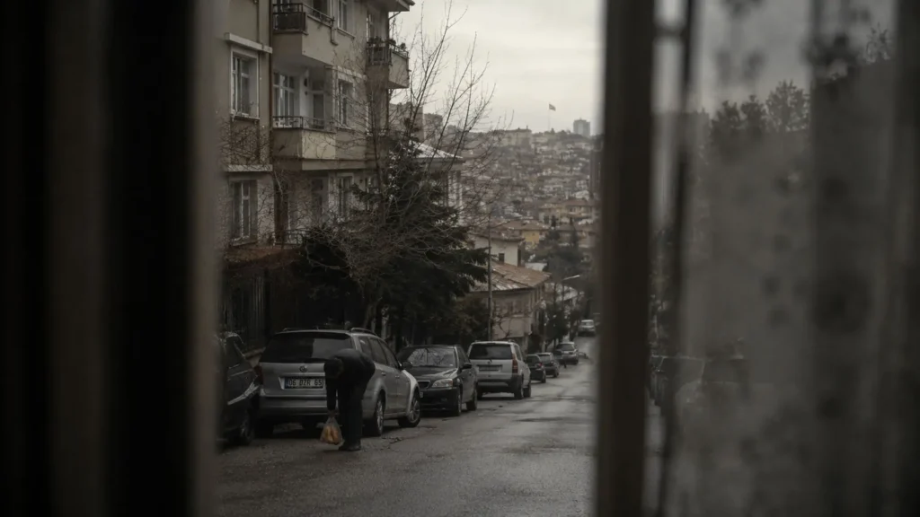 A quiet Ankara street seen through a window as a man bends to tie his shoe