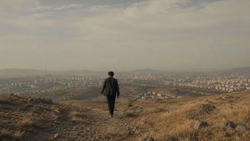 Barış walking down a dry hillside overlooking Ankara at sunset