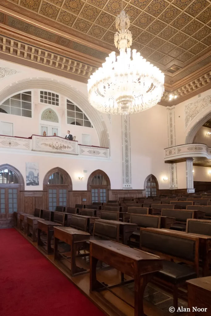 Historic parliamentary chamber inside Ankara Republic Museum, showing wooden benches, upper galleries, an ornate ceiling and a large chandelier.