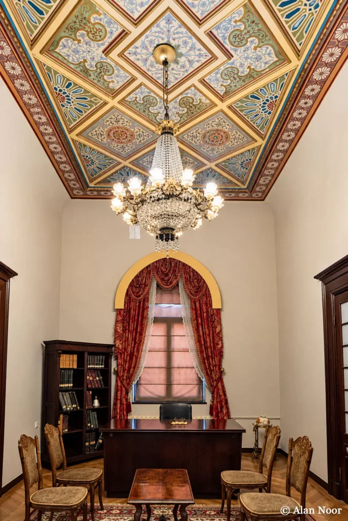 Historic office-style room at Ankara Republic Museum with a wooden desk, bookshelves, ornate painted ceiling, chandelier and red curtains.
