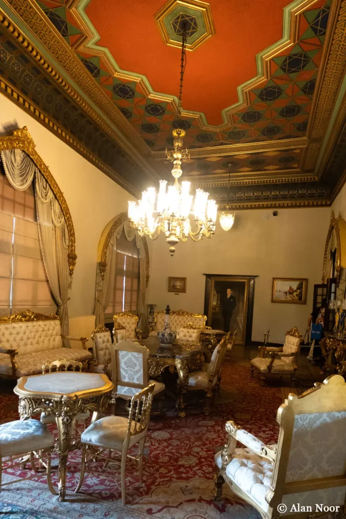 Ornate historic reception room at Ankara Republic Museum with gilded furniture, a chandelier, decorated ceiling and red patterned carpet.